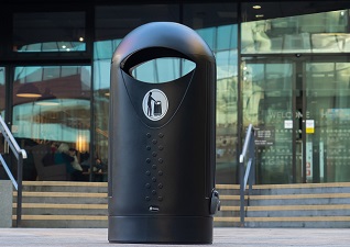 Poubelle urbaine Elipsa™ noir à l'extérieur d'un bâtiment professionnel