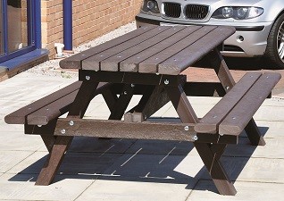 Clifton™ Recycled Material Picnic Table in brown, sited on paving slabs outside motorway facilities next to car park