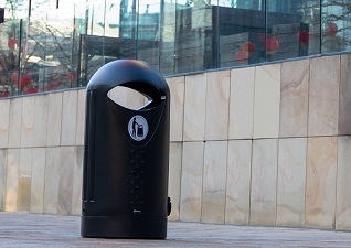 Elipsa™ Outdoor Litter Bin in black with white litter sticker in front of marble wall and glass building