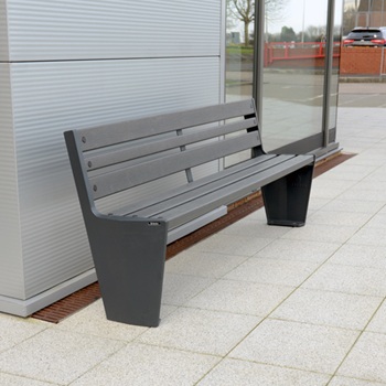 A bench placed against a grey wall with a glass window in the background