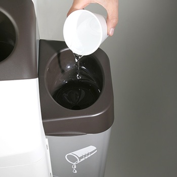 Een hand giet vloeistof uit een witte beker van kunststof of papier in het vloeistofreservoir van een recyclingbak.