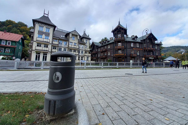 Kosz na śmieci Mini Plaza na betonowej podstawie i przechodzący ludzie