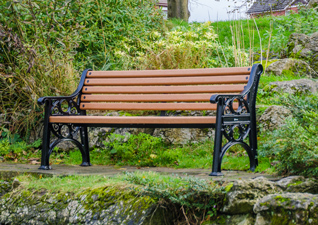 A light brown bench with black seat ends in a green space