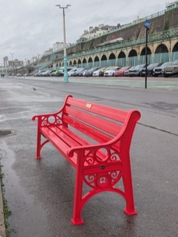 side view of a red british heart foundation bench on a seaside promenade