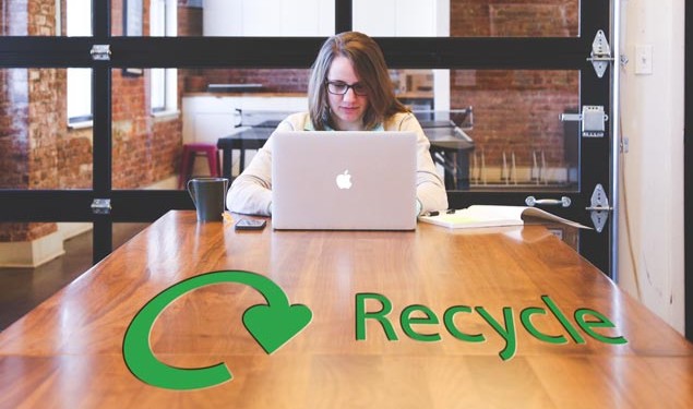 lady in a modern office working on a laptop with a recycling sign on the table in front of her