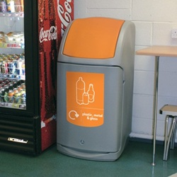 nexus 140 recycling bin with orange plastic, metal, and glass graphics in a staff room next to a drinks fridge