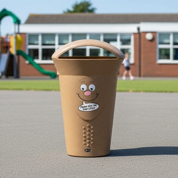 A light brown Glasdon bin with a smiley face billy bin-it graphic on it next to a school playground on a sunny day