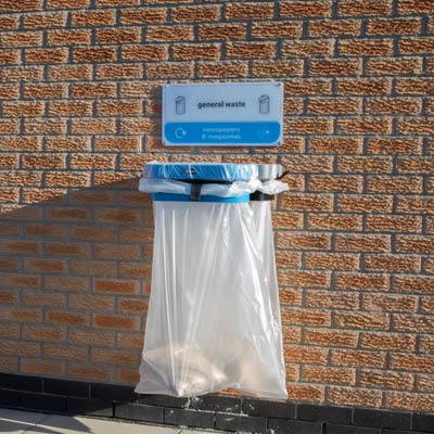 TSU transparent sack holder bin mounted to a brick wall in outdoor public space