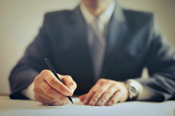 Someone sat at a desk signing a peice of paper