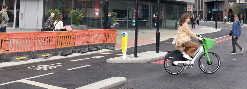 a cyclist and pedestrians using active travel infrastructure in an urban city centre