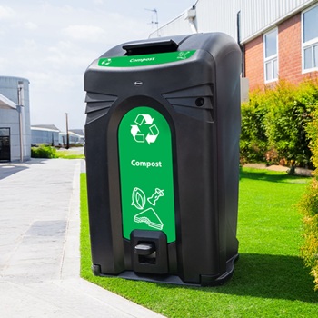 A large food waste bin housing for a wheelie bin in a public space, surrounded by green grass and near a footpath