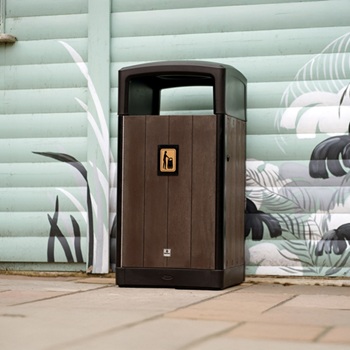 A large brown garbage can against a wall with illustrations on a beach front